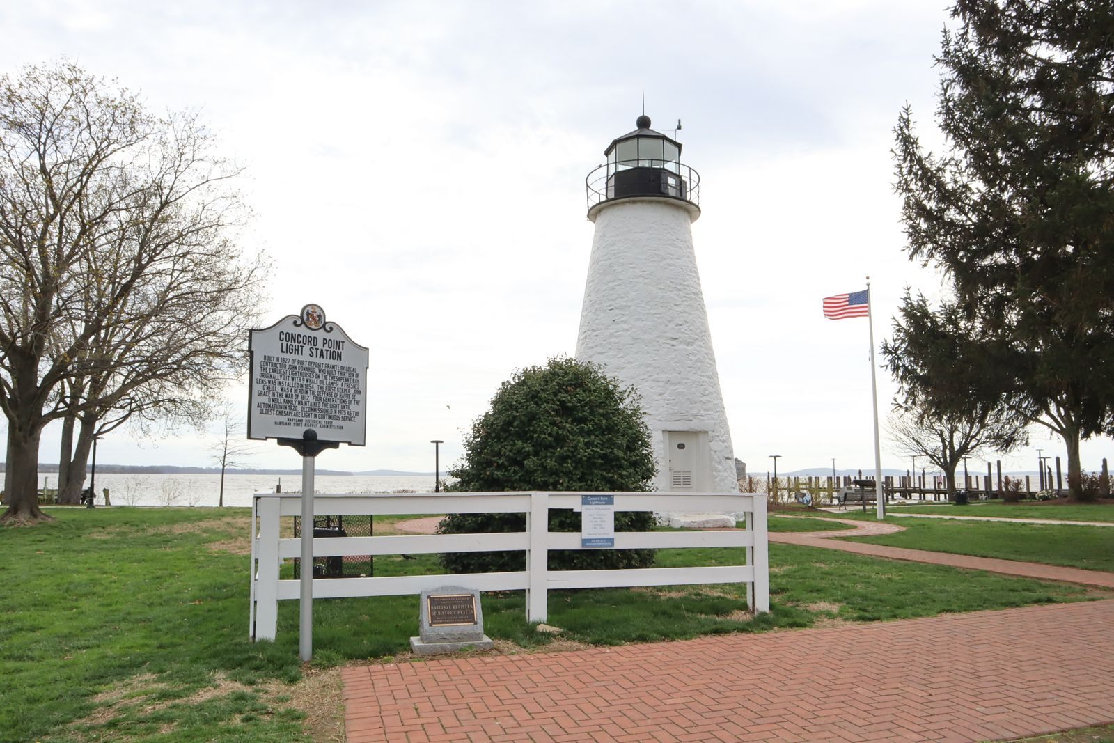 Historic lighthouse with an American flag beside calm water